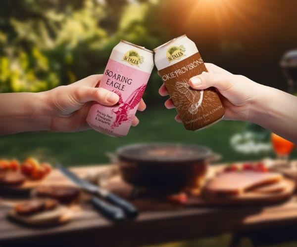 St. Tales Zero-Alcohol Drinks – Soaring Eagle and Okie Provisions Outdoor Toast Two hands raising St. Tales zero-alcohol cans of Soaring Eagle and Okie Provisions during an outdoor BBQ meal
