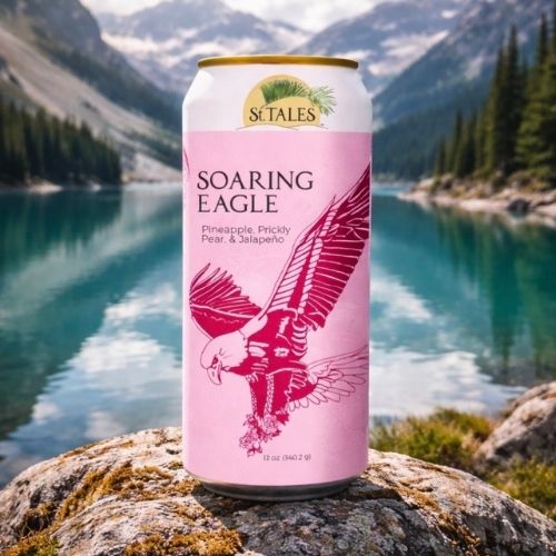 Soaring Eagle Zero-Alcohol Beverage – Pineapple, Prickly Pear & Jalapeño with Eagle St. Tales Soaring Eagle zero-proof can with eagle illustration and tropical flavors set before a clear mountain lake.